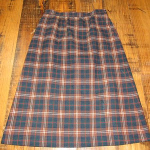 May include: A knee-length plaid skirt in shades of brown, navy, red, and white. The skirt features a classic tartan pattern and a gathered waistband. The fabric appears to be a medium-weight material, suitable for cooler weather.