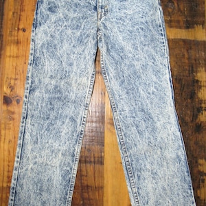 May include: Acid wash denim jeans with a classic five-pocket design. The jeans have a light blue and white marbled pattern, a button and zipper closure, and a straight leg cut. A vintage style.