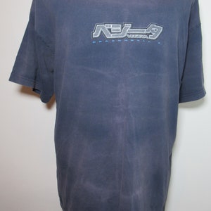 May include: A faded blue t-shirt featuring the text "Vegeta" in a stylized font, with Japanese characters above. The shirt has a crew neck and short sleeves. The text "Dragonball" is below the name.