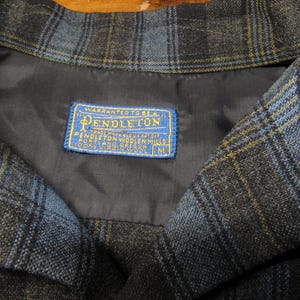 K&ouml;nnte beinhalten: Nahaufnahme eines Kragens einer blau, schwarz und gelb karierten Jacke. Die Jacke hat ein dunkelblaues Futter und ein blau-gelbes Etikett mit der Aufschrift "Pendleton" und "100% Virgin Wool". Die Jacke hat die Gr&ouml;&szlig;e M.