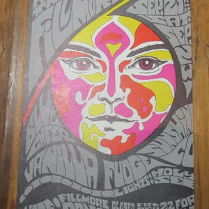 May include: A vintage concert poster with a colourful, stylized face design in pink, yellow, and orange. The grey background features swirling text, including "Fillmore" and "Donovan". The poster advertises a concert at the Palace.