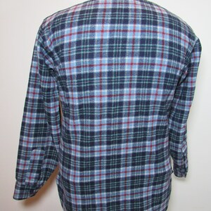 May include: A long-sleeved flannel shirt in a traditional plaid design. The shirt displays a colour palette of navy blue, light blue, green, and red. The shirt is buttoned and has a collar.