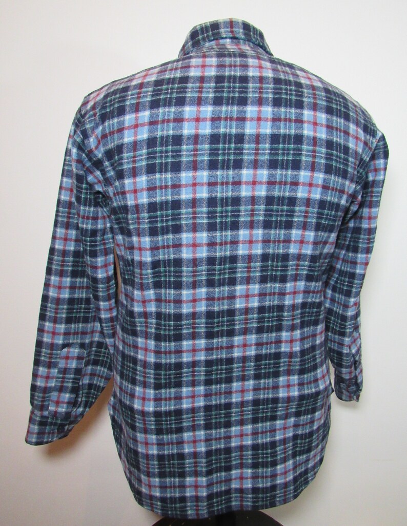 May include: A long-sleeved flannel shirt in a traditional plaid design. The shirt displays a colour palette of navy blue, light blue, green, and red. The shirt is buttoned and has a collar.