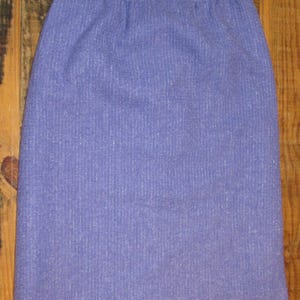 May include: A purple skirt made of a textured fabric. The skirt has a straight cut and a waistband.
