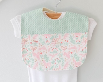 May include: A white baby onesie with a green and pink patterned bib attached. The bib has a geometric pattern on the top and a floral pattern on the bottom.