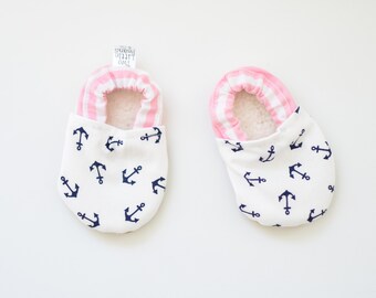 May include: A pair of white baby booties with a pink and white striped cuff. The booties have a navy blue anchor pattern.