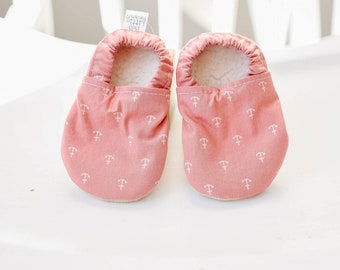 May include: A pair of pink baby booties with a white anchor print. The booties are made of soft fabric and have a fleece lining. The tag on the booties reads "Two Little Beans".