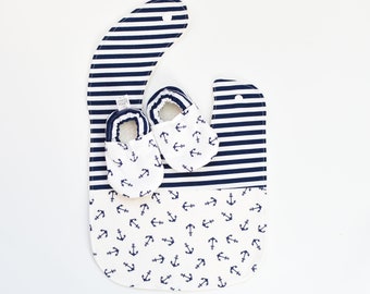 May include: A white and blue striped bib with a pocket and a pair of white baby booties with a navy blue anchor print.
