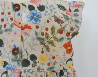 May include: A sleeveless dress with a floral print featuring strawberries, butterflies, and flowers in shades of pink, blue, yellow, green, and red. The dress has a ruffled neckline and a button closure in the front.