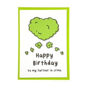 May include: A white greeting card with a green border features a green cloud illustration and the words "Happy Birthday to my fartner in crime" in black text. The card is rectangular.