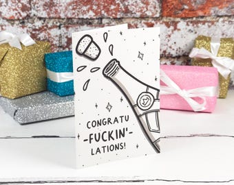 Könnte beinhalten: Eine weiße Grußkarte mit einer schwarz-grauen Strichzeichnung einer Champagnerflasche, deren Korken herausspringt. Der Text auf der Karte lautet CONGRATU-FUCKIN'-LATIONS! in fetten schwarzen Großbuchstaben, umgeben von kleinen Stern- und Tropfensymbolen.
