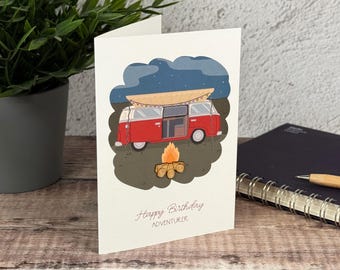 Könnte beinhalten: Eine weiße Grußkarte mit einem roten Campingbus, der ein Surfbrett auf dem Dach trägt und nachts neben einem Lagerfeuer steht. Der Text auf der Karte lautet Happy Birthday ADVENTURER in einer einfachen Schrift. Das Motiv ist vor einem Nachthimmel.
