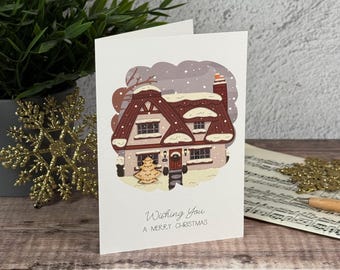 Könnte beinhalten: Eine weiße Grußkarte mit einer zentralen Illustration eines zweistöckigen Hauses mit schneebedecktem, dunkelrotem Dach, umgeben von einer hellvioletten Wolkenform. Unter dem Haus steht der Text Wishing You A MERRY CHRISTMAS in Schwarz.