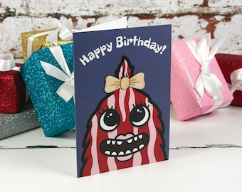 Könnte beinhalten: Eine dunkelblaue Grußkarte mit dem Text Happy Birthday! und einer Illustration eines rot-rosa gestreiften Monsters mit einer beigen Schleife. Die Karte steht vor mehreren glitzernden Geschenkboxen, die mit weißen Satinbändern verziert sind.