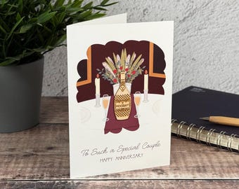 Könnte beinhalten: Eine weiße Grußkarte mit einer zentralen Illustration einer Champagnerflasche mit der Aufschrift HOORAY, zwei Gläsern, Kerzen und einem Blumenarrangement auf einem Tisch. Der Text lautet To Such a Special Couple HAPPY ANNIVERSARY.
