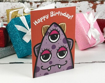 Könnte beinhalten: Eine Grußkarte mit rostorangem Hintergrund und einer Illustration eines violetten, dreiäugigen Monsters mit dunkelvioletten Punkten, rosa Augenlidern und weißen Fangzähnen. Der Text Happy Birthday ist oben in Weiß aufgedruckt.