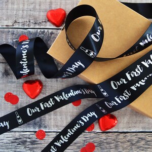 May include: Black satin ribbon with silver lettering that reads "Our First Valentine's Day" and a champagne bottle graphic.