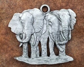 May include: A silver pewter ornament featuring three elephants standing side-by-side. The elephants are facing forward with their trunks raised.