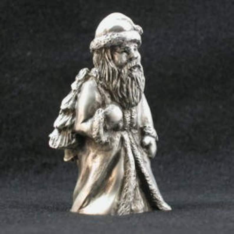 May include: A silver figurine of Santa Claus holding a bag of presents. He is wearing a red hat and a white beard.