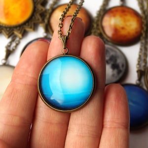 May include: A set of nine necklaces featuring different planets of the solar system. Each necklace has a round pendant with a detailed image of a planet, including Saturn, Jupiter, Mars, and Earth. The pendants are made of glass and have a bronze-colored metal frame.