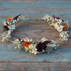 May include: A dried flower crown featuring white, burgundy, orange, and yellow blooms. The crown is crafted with a natural vine base.
