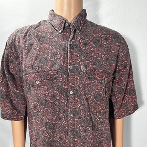 May include: A short-sleeved button-down shirt with a paisley print in shades of black and pink.