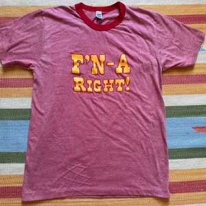 May include: A red heather t-shirt with a red and white ringer neck. The shirt has a yellow graphic that says "F'N-A RIGHT!"