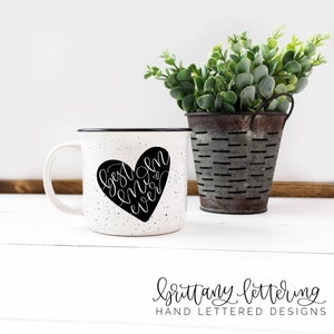Może przedstawiać: Biały, nakrapiany ceramiczny kubek z czarną obw&oacute;dką i uchwytem. Czarny serce z napisem "best mom ever" znajduje się na kubku. Mały metalowy kubełek z zielenią stoi po prawej stronie kubka.