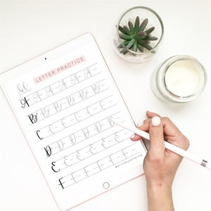 May include: A digital tablet showing a calligraphy practice sheet with the words "LETTER PRACTICE." The sheet displays the letters A to F in a cursive style. A hand holding a stylus is visible, along with a small succulent and a candle.
