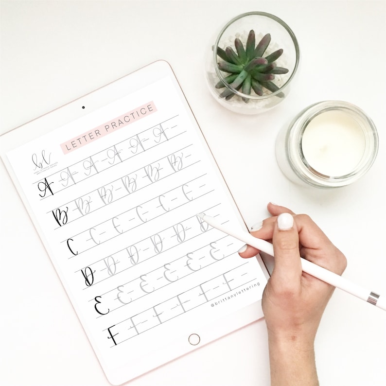 May include: A digital tablet showing a calligraphy practice sheet with the words "LETTER PRACTICE." The sheet displays the letters A to F in a cursive style. A hand holding a stylus is visible, along with a small succulent and a candle.