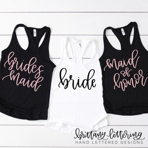 以下が含まれることがあります： 結婚式のパーティー用のタンクトップ3枚。中央に黒い文字で「bride」と書かれた白いタンクトップがあります。その両側には、ピンクの文字で「bridesmaid」と「maid of honor」と書かれた黒いタンクトップがあります。
