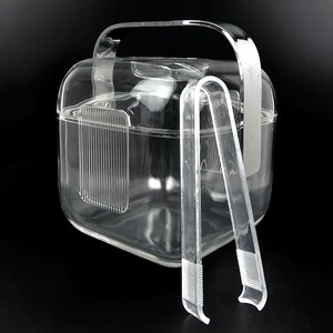 May include: A transparent, square ice bucket with a handle and matching tongs. The bucket has a lid and a vertical, ridged design on the side. The tongs are resting against the bucket.
