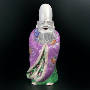 May include: A porcelain figurine of a Chinese deity, with a white head and a purple robe with floral designs. The deity has a white beard and a smiling face.