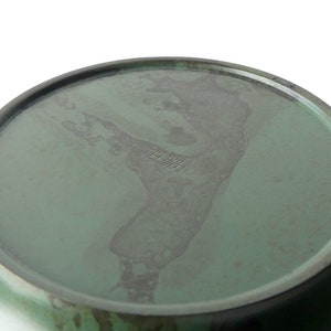 May include: The bottom of a green ceramic bowl with a dark green glaze. The bowl has a mark on the bottom that reads "The New"