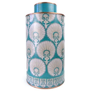 Può includere: Un contenitore decorativo cilindrico turchese e bianco con coperchio. Il contenitore presenta un motivo ripetuto di forme a ventaglio stilizzate e una fascia decorativa alla base. Il bordo e il coperchio sono rifiniti con metallo color oro.