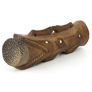 以下が含まれることがあります： 複雑なデザインと象嵌された白いアクセントが施された、彫刻された木製の枕。枕は魚の形をしており、表面は質感があります。