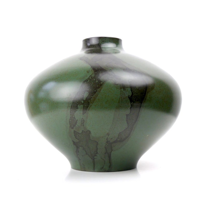 May include: A green ceramic vase with a dark green and black marbled design. The vase has a wide, round base and a narrow neck.
