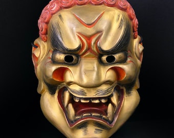 May include: A traditional Japanese Noh mask with a fierce expression. The mask is painted in gold, red, and black, with detailed features and a wide open mouth. The mask is made of wood and has a textured surface.