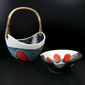 May include: Two ceramic bowls with a distinctive design. One bowl has a woven handle. The bowls feature a white top, teal middle, and red accents. The interior of the bowls has a glossy finish with green and blue hues. The bowls are on a black background.
