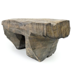 May include: A rustic wooden stool with a unique, asymmetrical design. The stool is made of dark brown wood and has a rough, textured surface.
