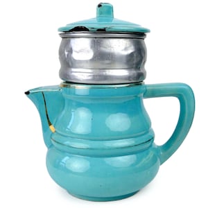 Könnte beinhalten: Eine türkisfarbene Vintage-Kaffeekanne mit einem silbernen Filter und Deckel. Die Kanne hat einen Griff und einen Ausguss, mit einer goldfarbenen Reparatur an der Seite. Deckel und Kanne weisen Gebrauchsspuren auf.