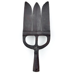 Puede incluir: Una cabeza de tridente de metal gris oscuro y desgastado con tres puntas planas que se extienden desde una barra horizontal central. Debajo de la barra, la estructura incluye dos aberturas redondeadas que conducen a un casquillo cilíndrico con un pequeño orificio.