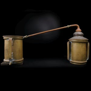 Può includere: Un alambicco in ottone con un tubo di rame che collega due contenitori rotondi. L'alambicco è su uno sfondo nero.