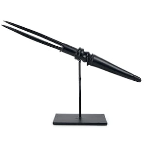 Puede incluir: Un tenedor de metal negro con dos púas, montado en un soporte de metal negro. El tenedor está inclinado hacia arriba y el soporte tiene una base rectangular.