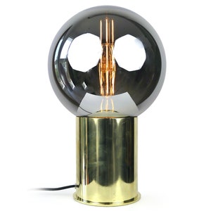 May include: A gold table lamp with a smoked glass globe shade. The lamp has a simple design and a classic look.