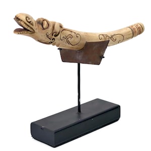 May include: A carved, cream-coloured sculpture of a stylized dragon or serpent, mounted on a black stand. The sculpture features intricate etched details and a weathered appearance. The base is a rectangular block.