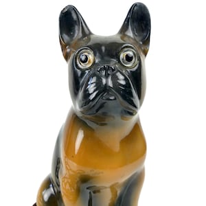 Könnte beinhalten: Keramikfigur eines französischen Bulldoggen. Der Hund hat eine glänzende Oberfläche mit schwarzen und braunen Farben. Der Hund sitzt aufrecht, die Ohren aufgestellt und die Augen nach vorne gerichtet.