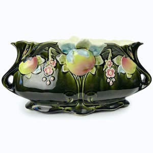 May include: A dark green ceramic planter with a glossy finish. The planter features raised relief designs of apples, leaves, and small pink flowers. The planter has a wide, oval shape with curved handles on each side.