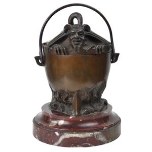 Peut inclure: Un récipient décoratif en bronze avec une poignée, orné d'une figure diabolique émergeant du haut. Le récipient repose sur une base en marbre rouge et blanc, mettant en valeur des détails complexes.