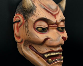 May include: A traditional Japanese demon mask with red and gold accents. The mask has horns, a wide mouth, and a fierce expression.